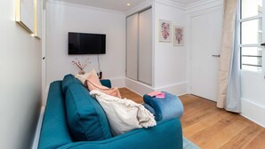 Ein Wohnzimmer mit einem türkisfarbenen Sofa, einem Flachbildfernseher und Kunstwerken an der Wand.