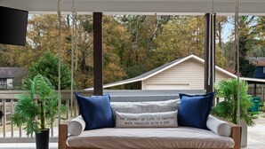 A porch with a swing seat, a potted plant, and a view of a house and trees. - Beautiful 3 bedroom ranch home in Smyrna near the Braves stadium  (Smyrna)