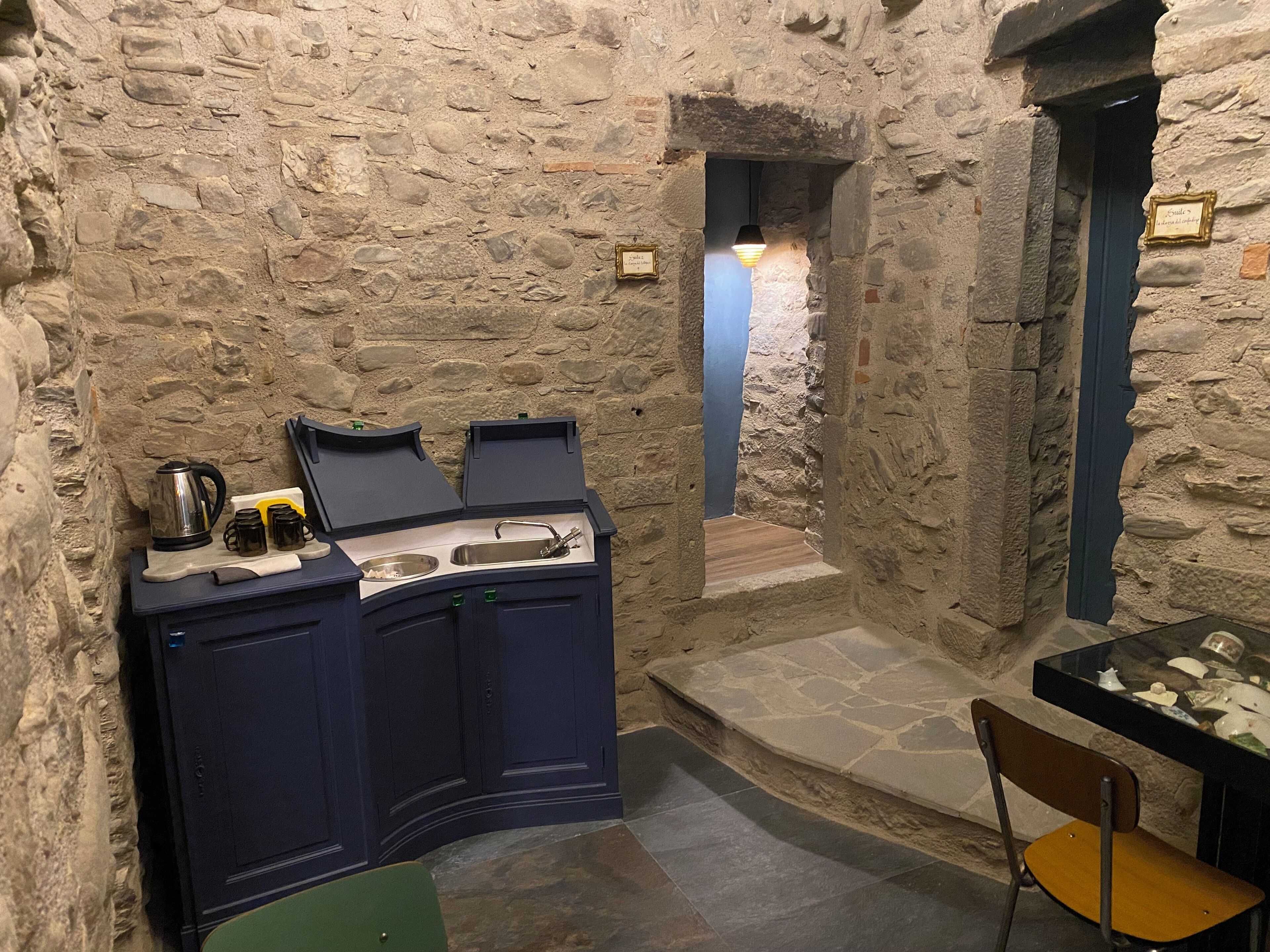 Une pièce aux murs de pierre dotée d’un coin cuisine intégré, comprenant un évier et une petite table avec une chaise.