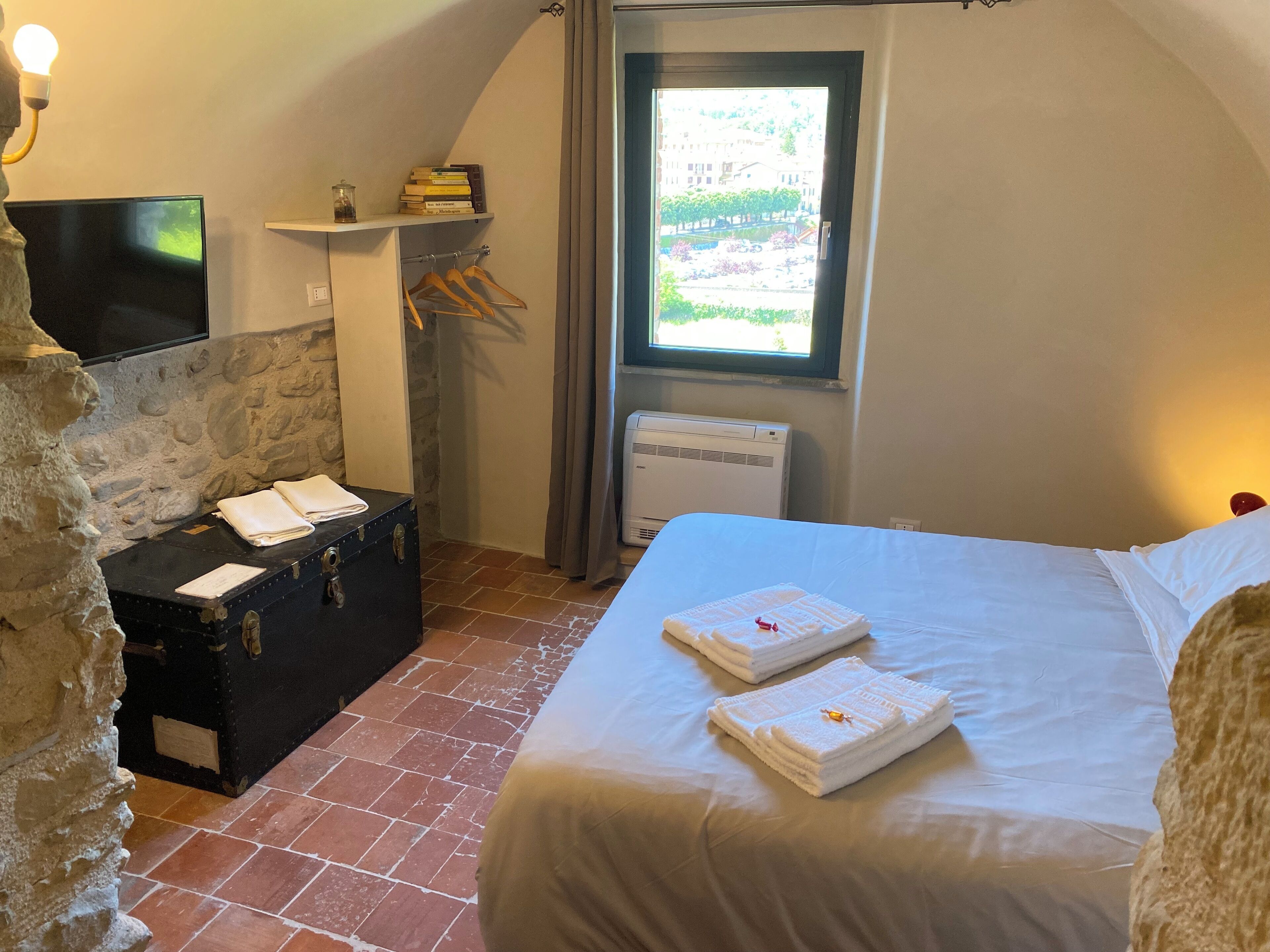 Un dormitorio con una cama, una maleta, un televisor, un calentador y una ventana con vistas.