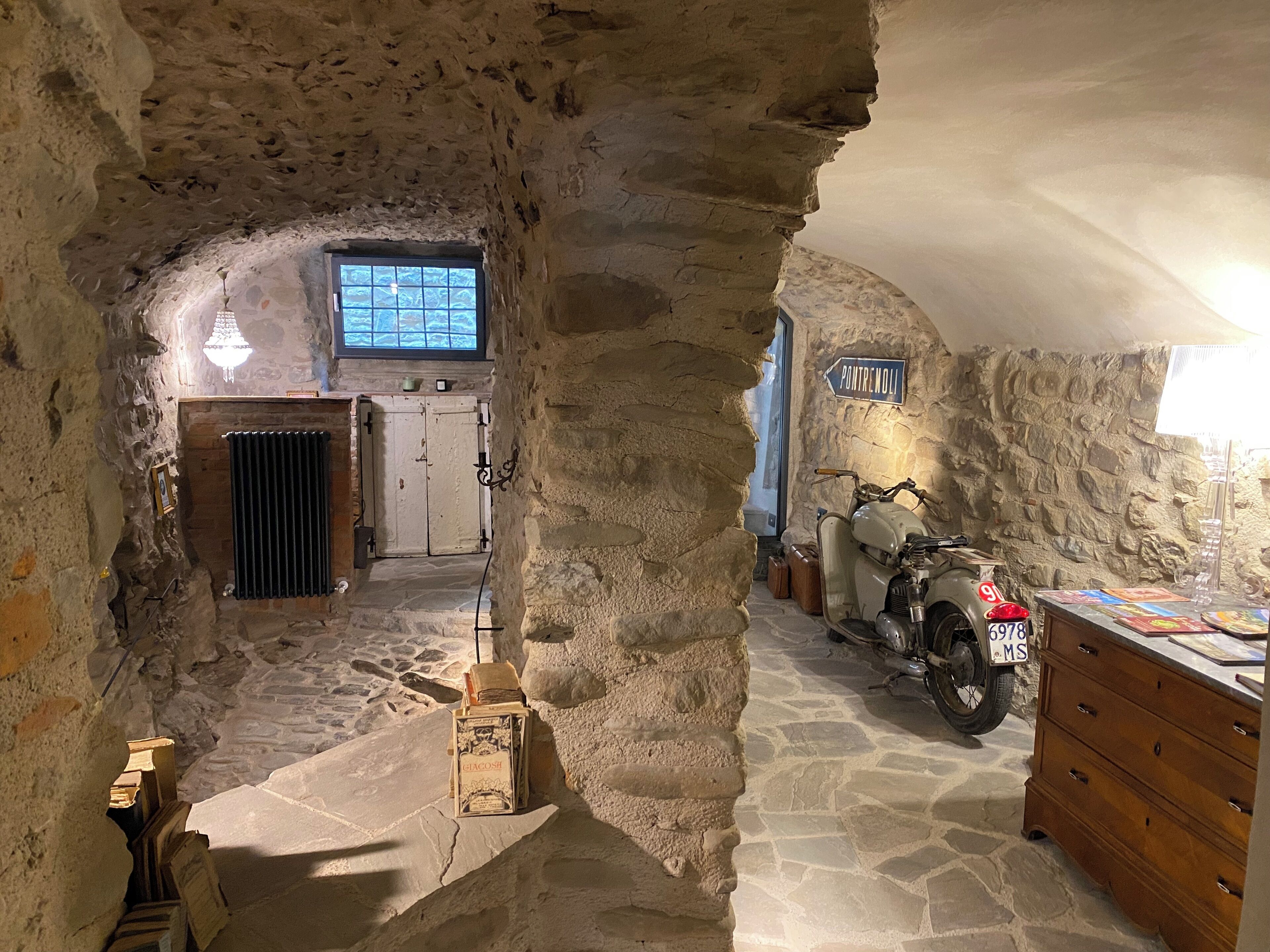 A stone-walled room with a motorcycle, a wooden dresser, and a window.