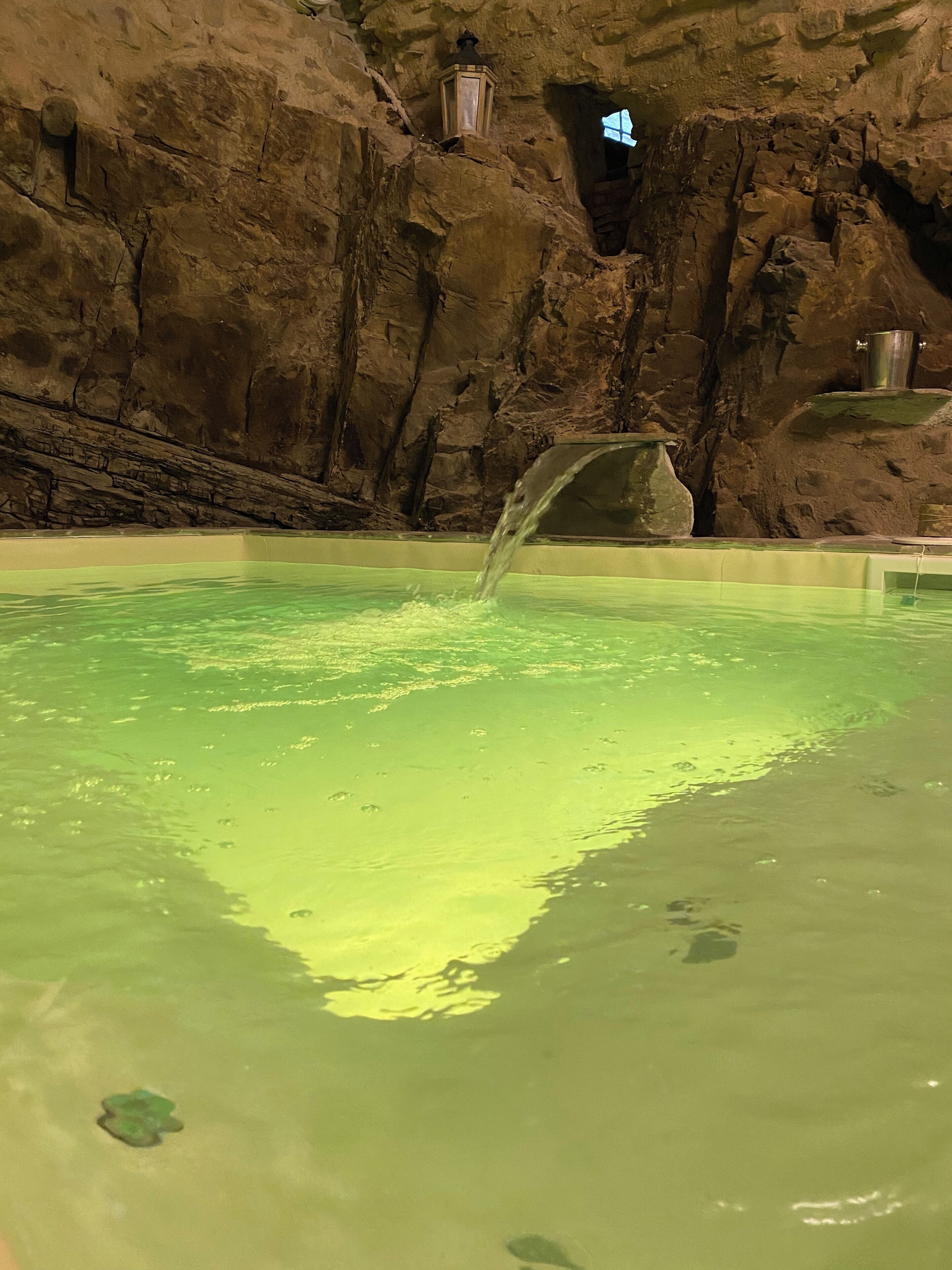 Une piscine à l’eau claire, un mur de pierre et une lanterne.
