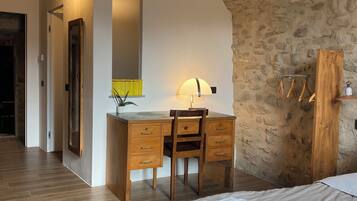 A bedroom with a wooden desk, a chair, a bed with neatly folded towels, and a stone wall.