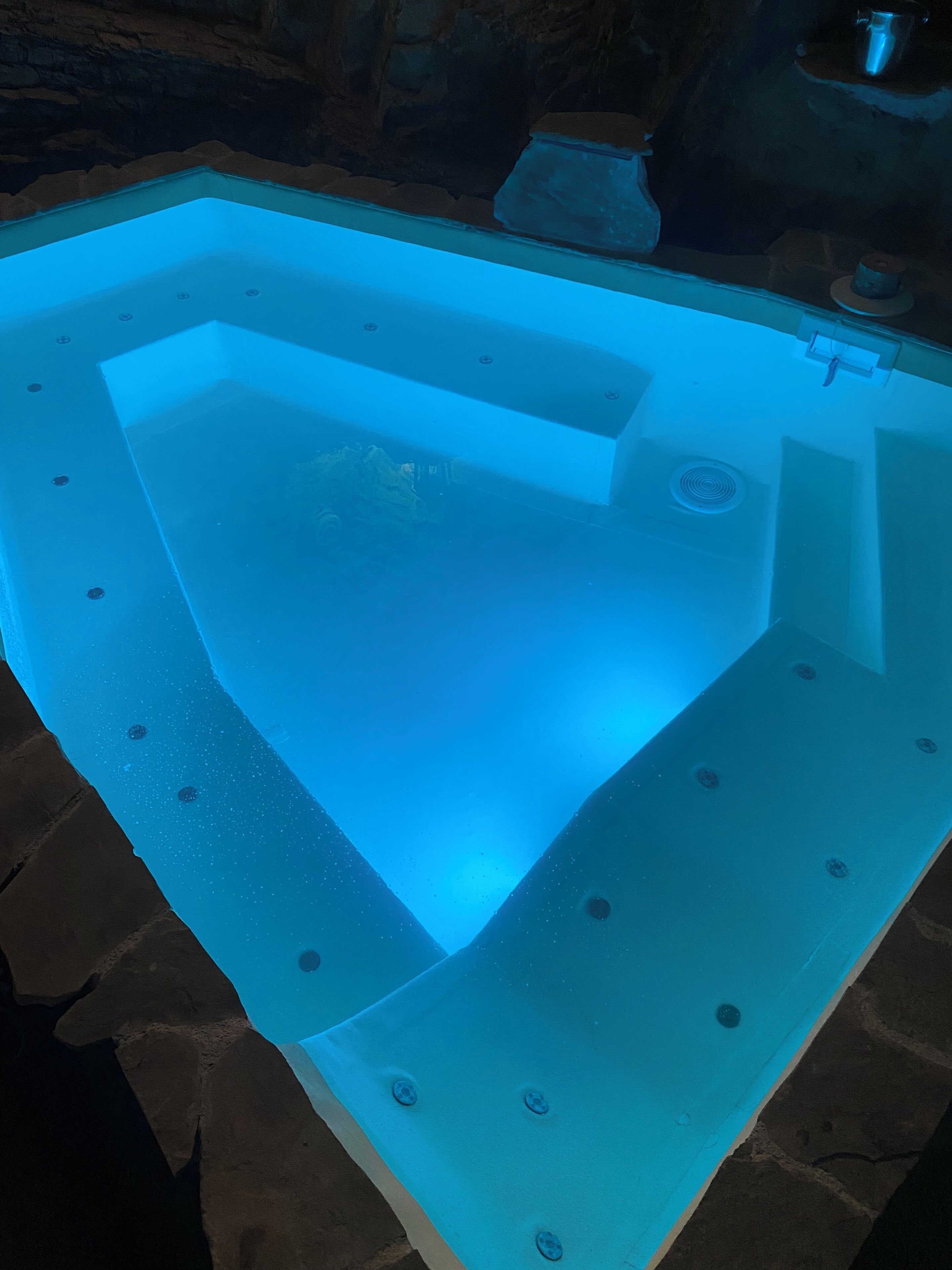 A swimming pool with a blue-lit interior, surrounded by stone tiles.