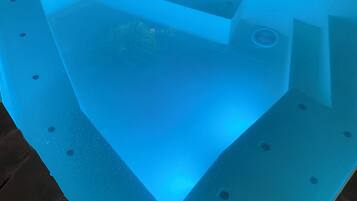 A swimming pool with a blue-lit interior, surrounded by stone tiles.