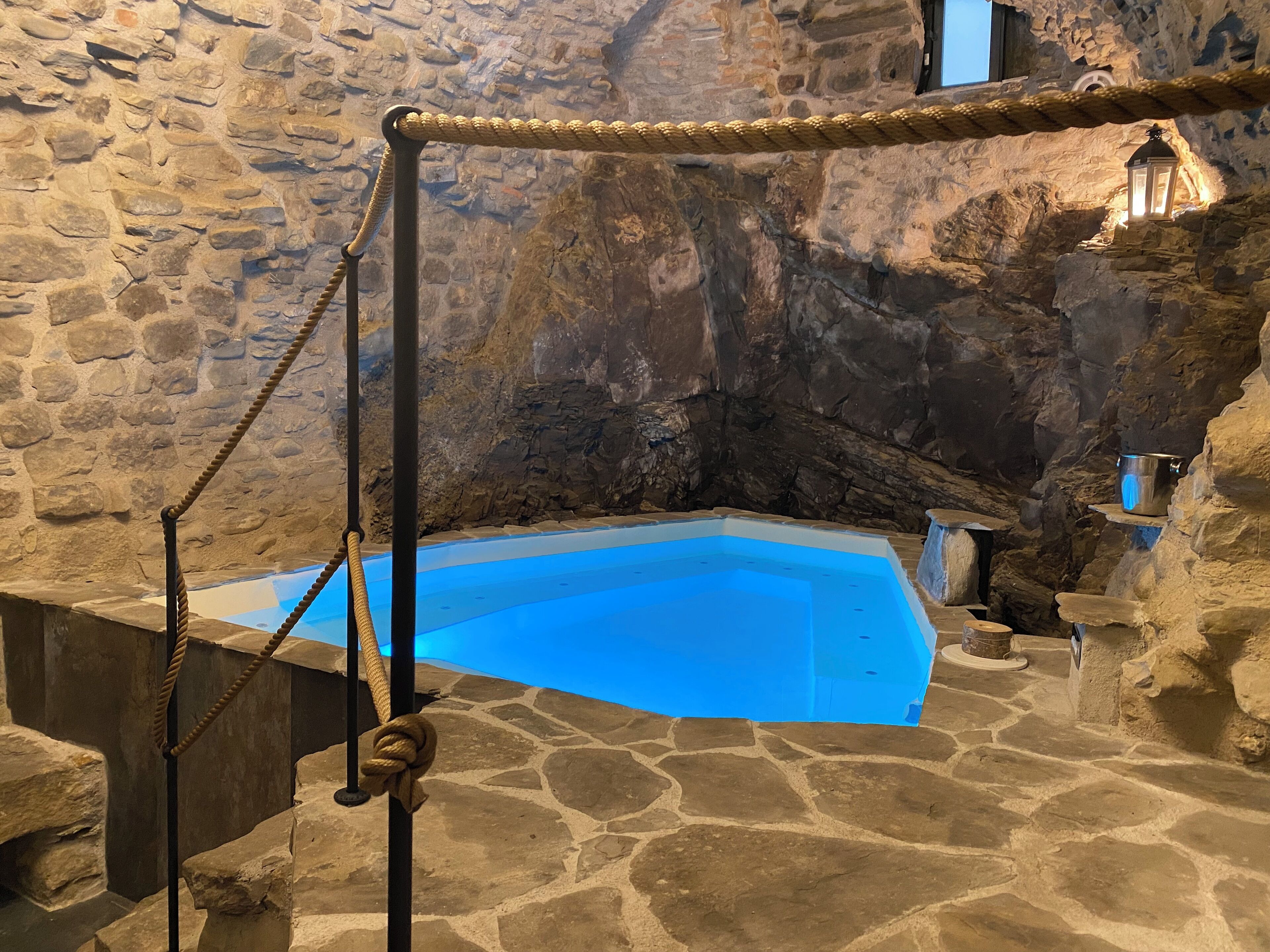 A stone-walled room with a blue pool, a rope barrier, and a lantern.