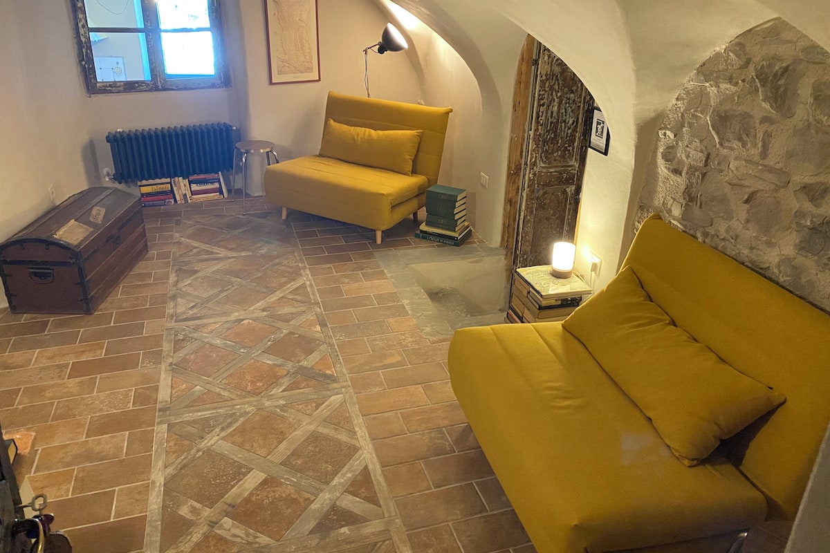 Een gezellige kamer met een gele bank, een vintage koffer en een stenen muur.