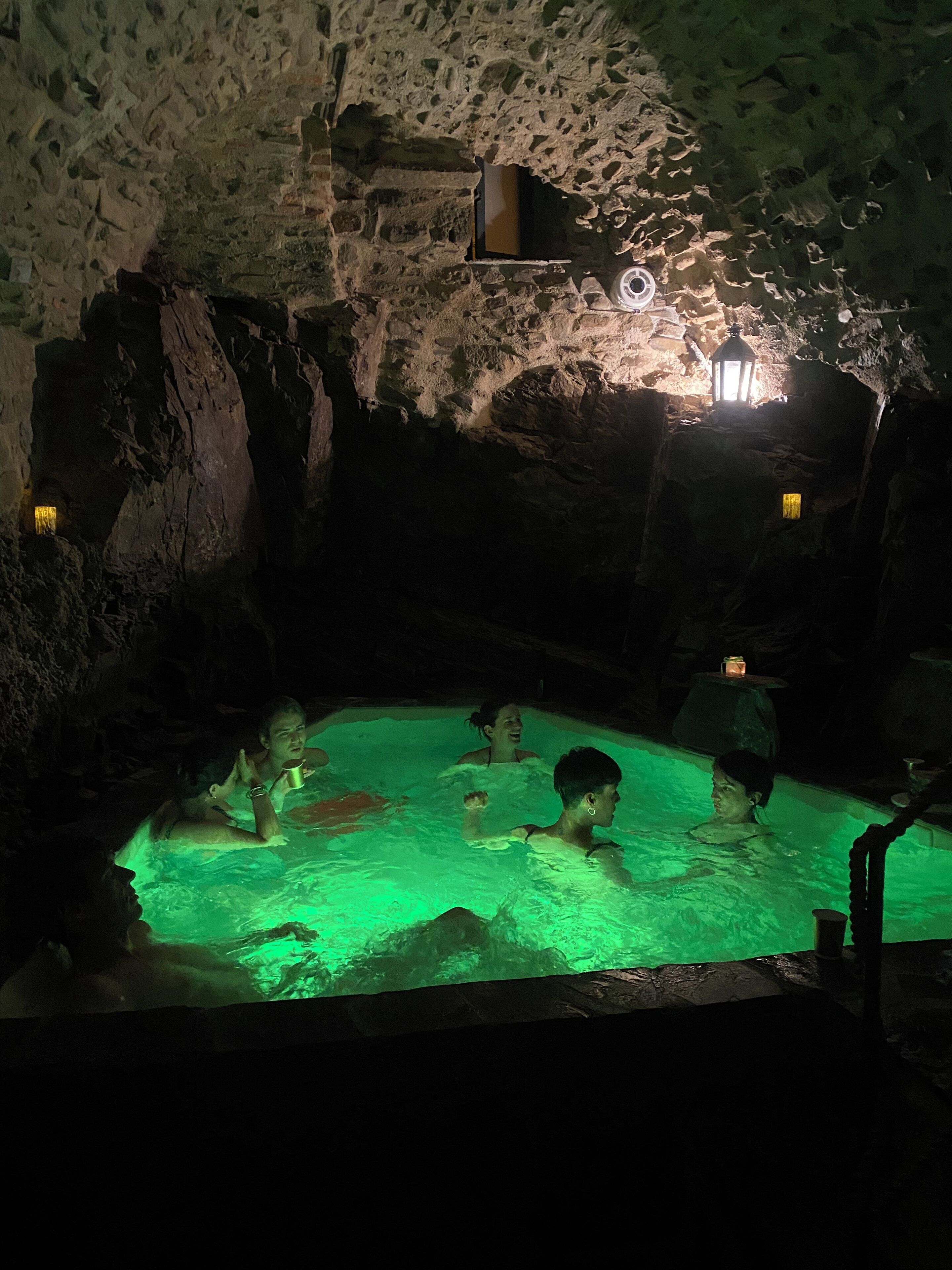 A cave-like pool with people swimming, illuminated by green lighting and lanterns.
