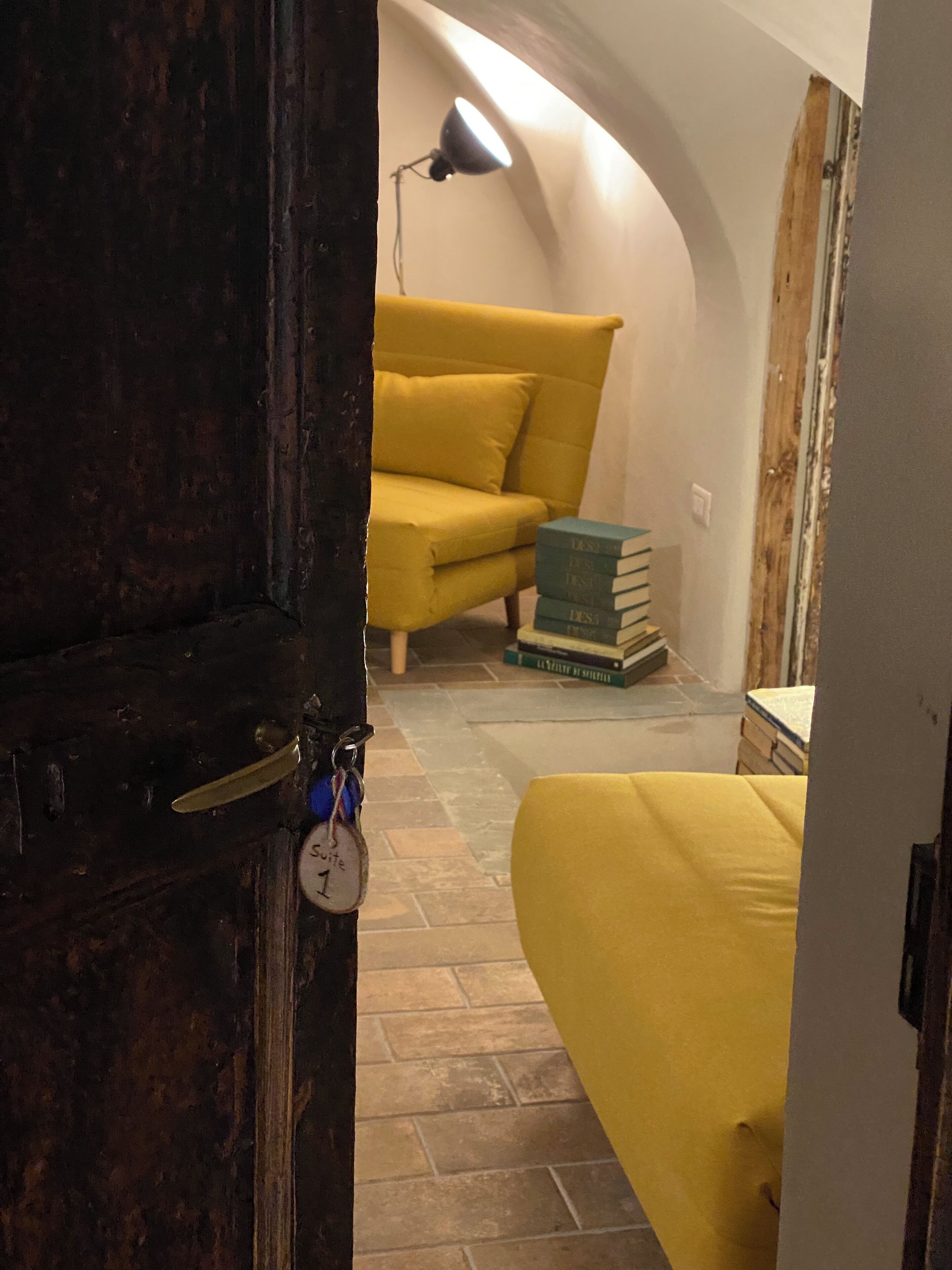 A room with a yellow sofa, a stack of books, and a lamp.