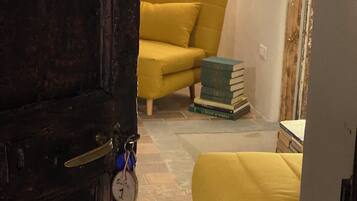 A room with a yellow sofa, a stack of books, and a lamp.