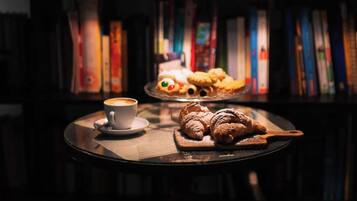 Um recanto acolhedor para leitura, com uma xícara de café e doces sobre uma mesa, cercado por estantes de livros.