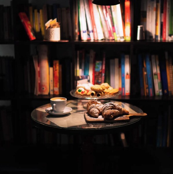 Un coin lecture confortable avec une tasse de café et des pâtisseries sur une table, entouré d’étagères à livres.