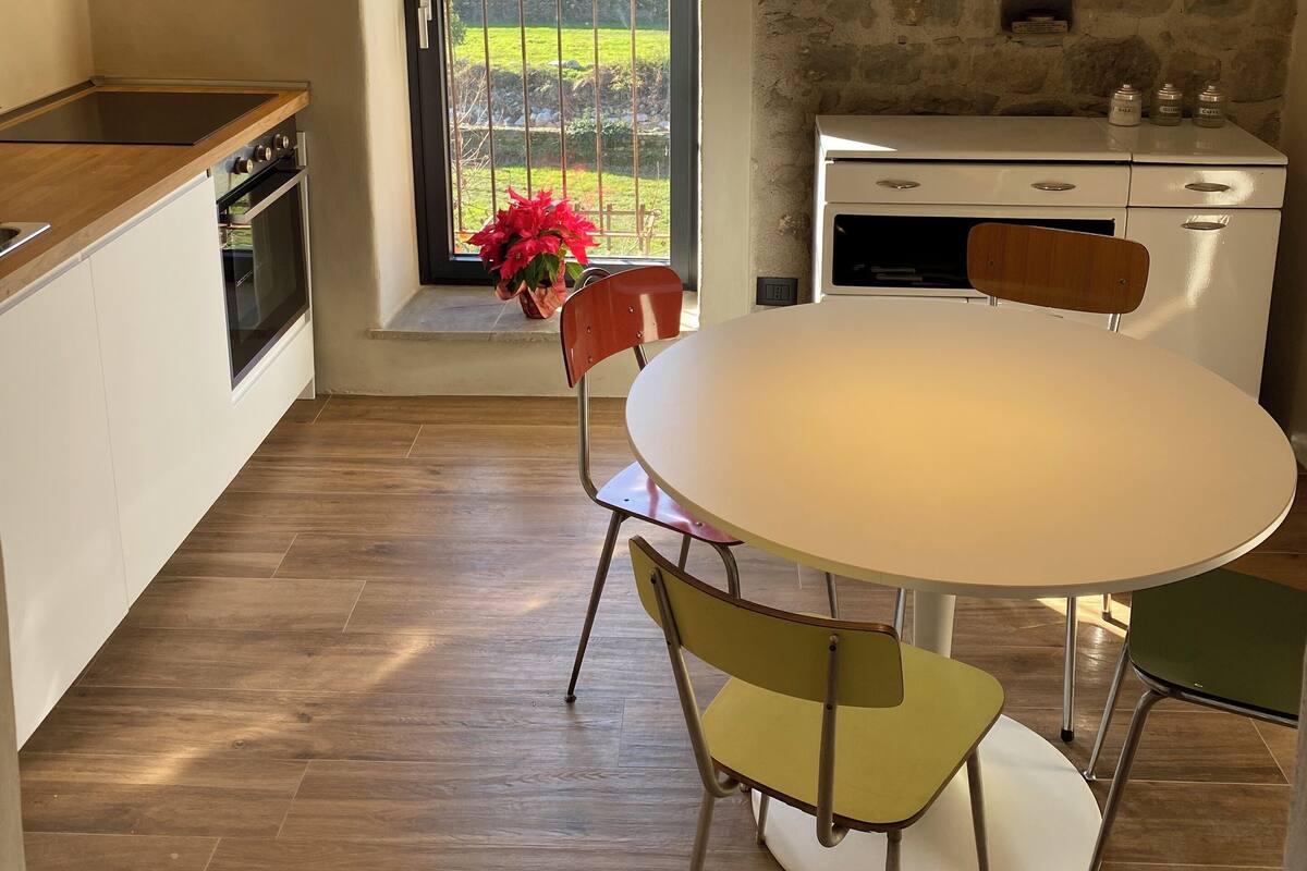 Een keuken met een stenen muur, een eettafel met stoelen en een uitzicht door een deur.