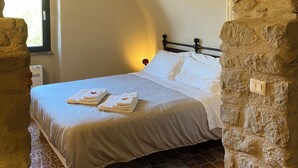 Een slaapkamer met een stenen boog, een bed met witte lakens en een raam met daglicht.