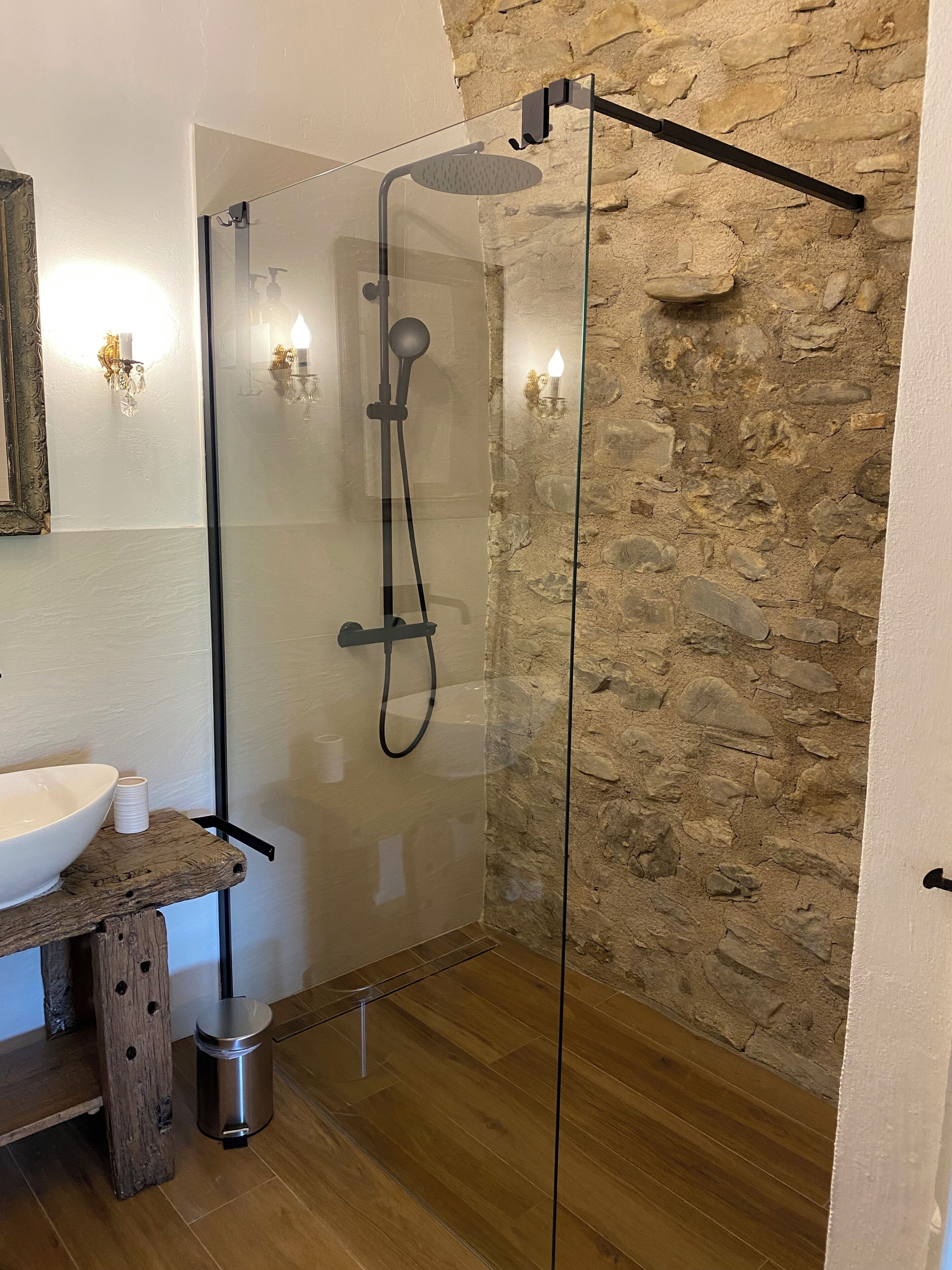 A modern bathroom with a stone wall, a glass-enclosed shower, a wooden vanity, and a white sink.