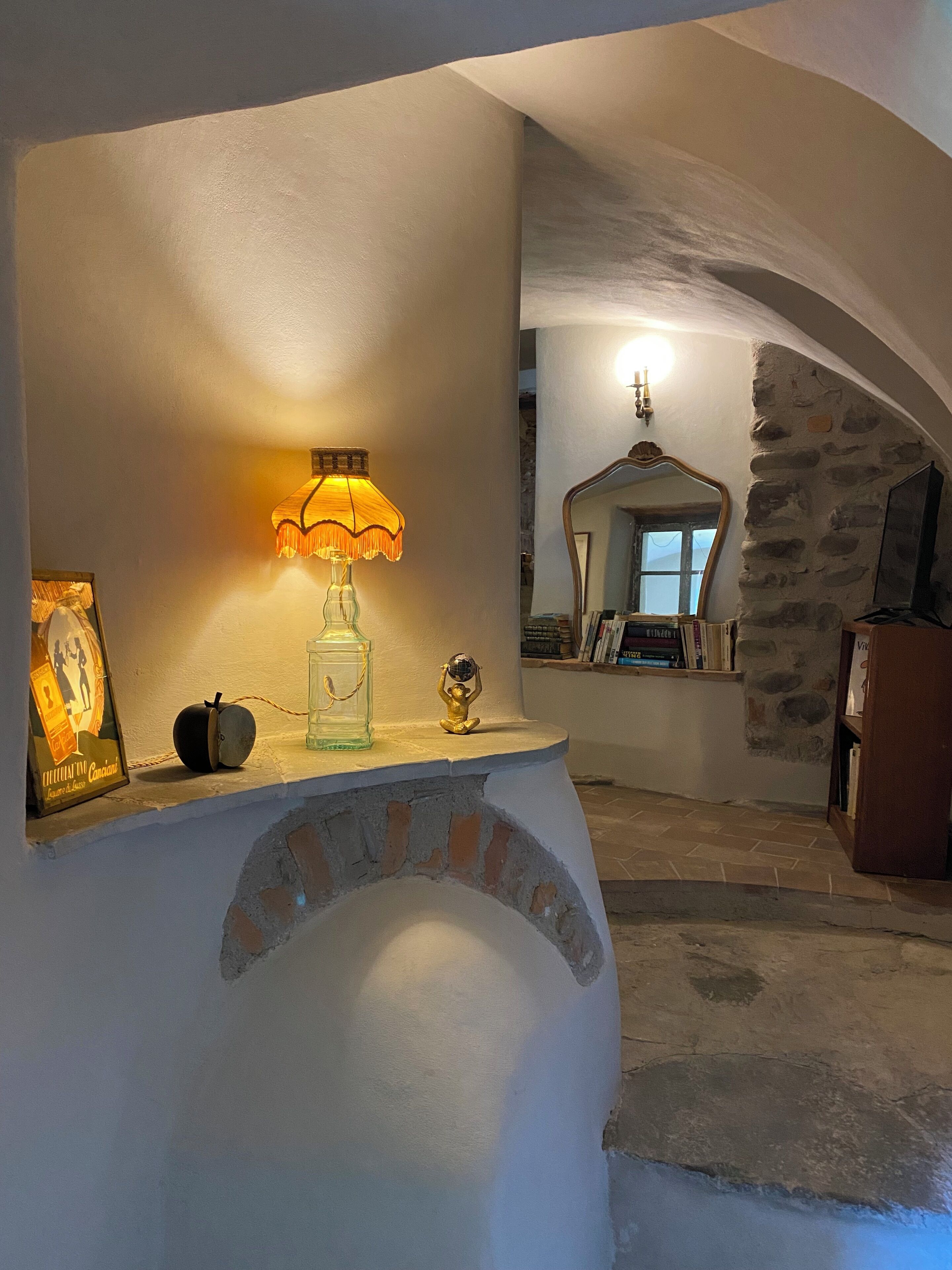 A cozy interior with a stone fireplace, a lit lamp, and a mirror reflecting a window.