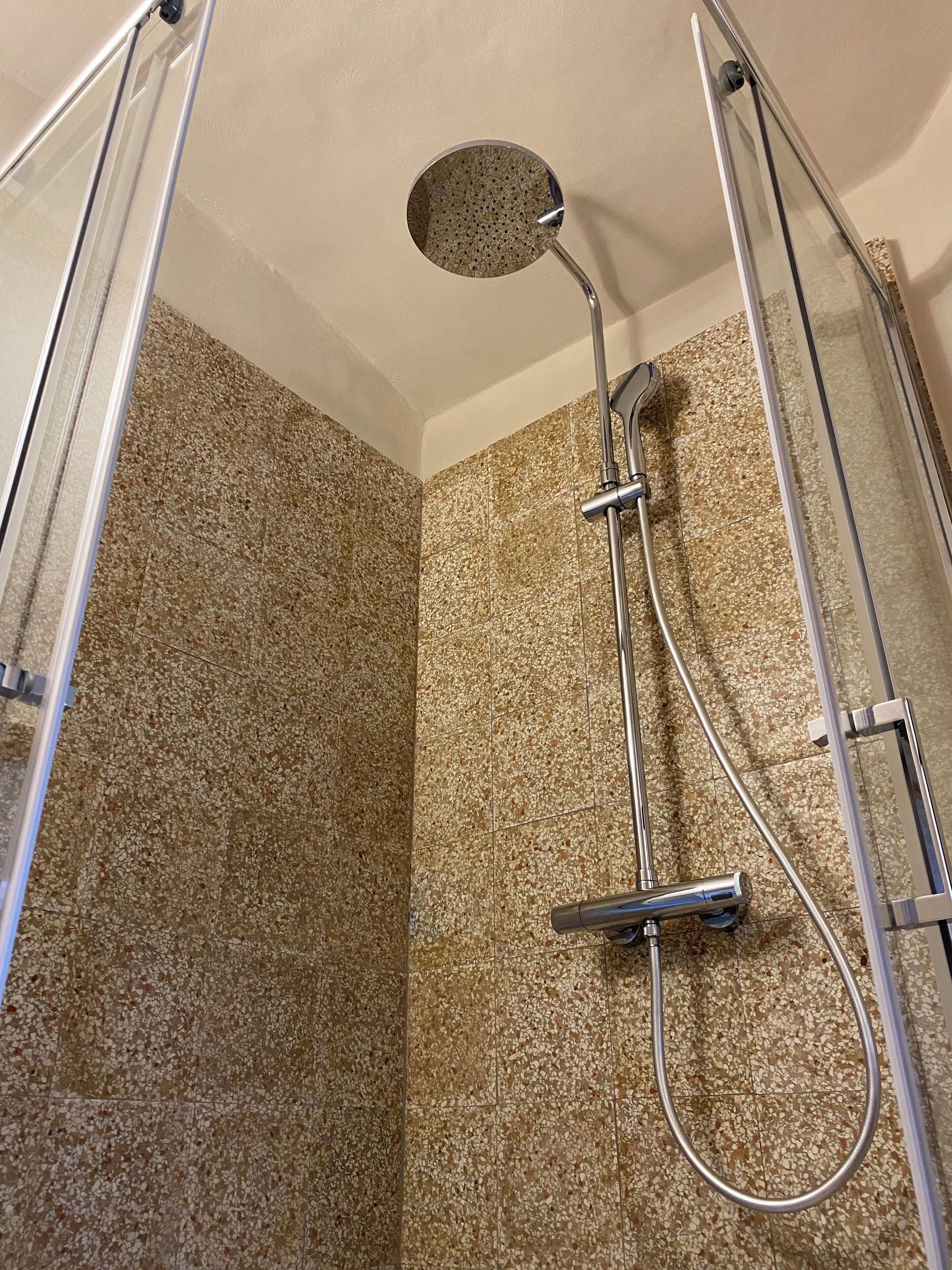 Ducha con cabezal de ducha de mano y cabezal de ducha tipo lluvia, ambos instalados en una estructura de cromo.