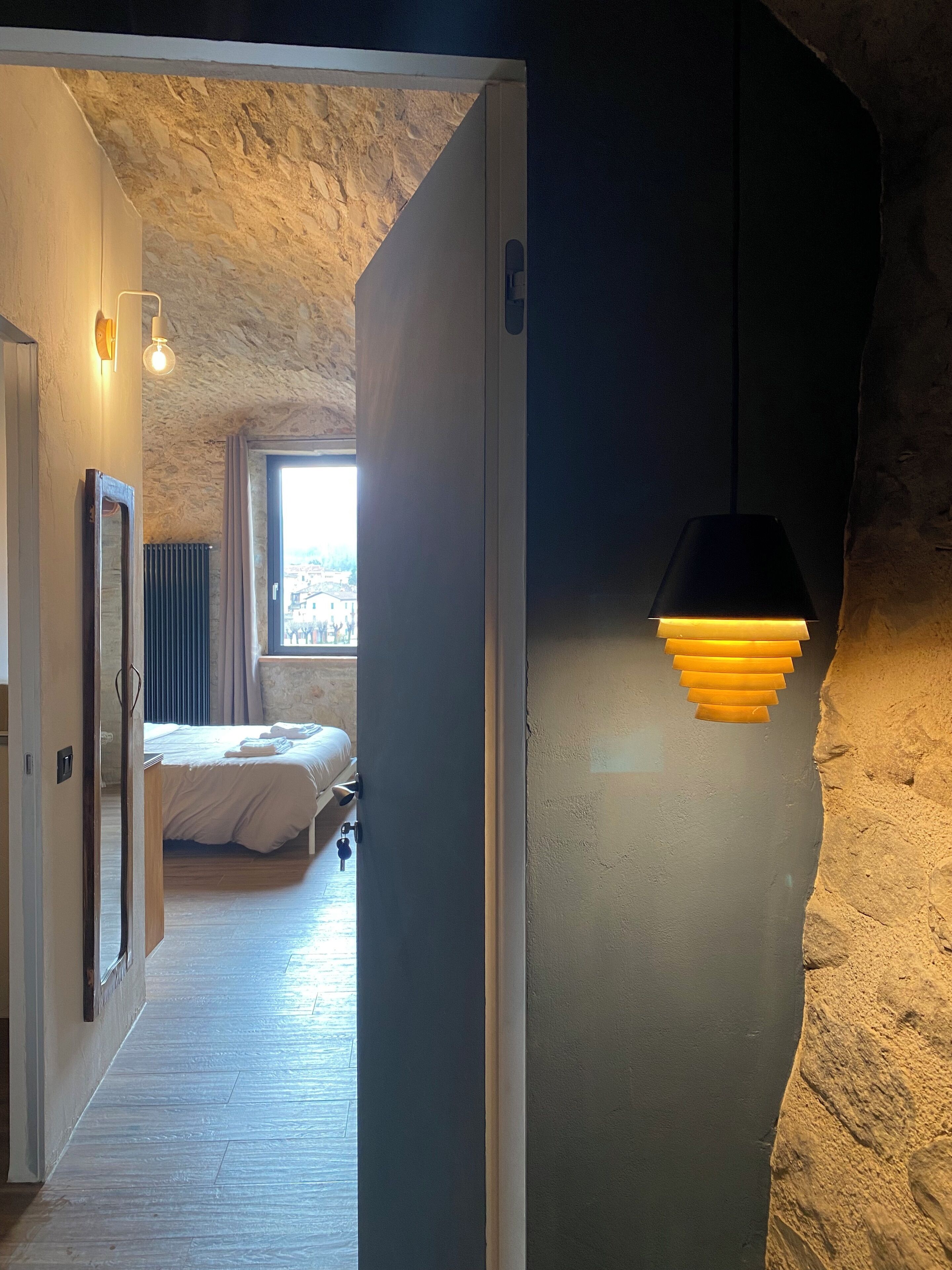 Une chambre moderne avec un mur en pierre, un lit et une lampe suspendue.