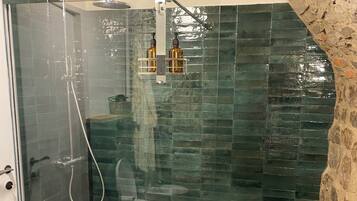 Une douche entièrementClose avec des parois en verre, un plancher en bois et un mur en pierre.