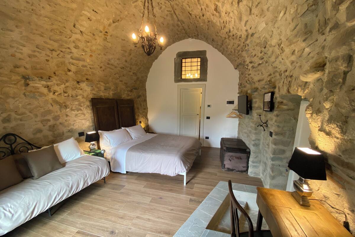 Een gezellige slaapkamer met een stenen muur, een houten bed, een bank en een bureau met lamp.