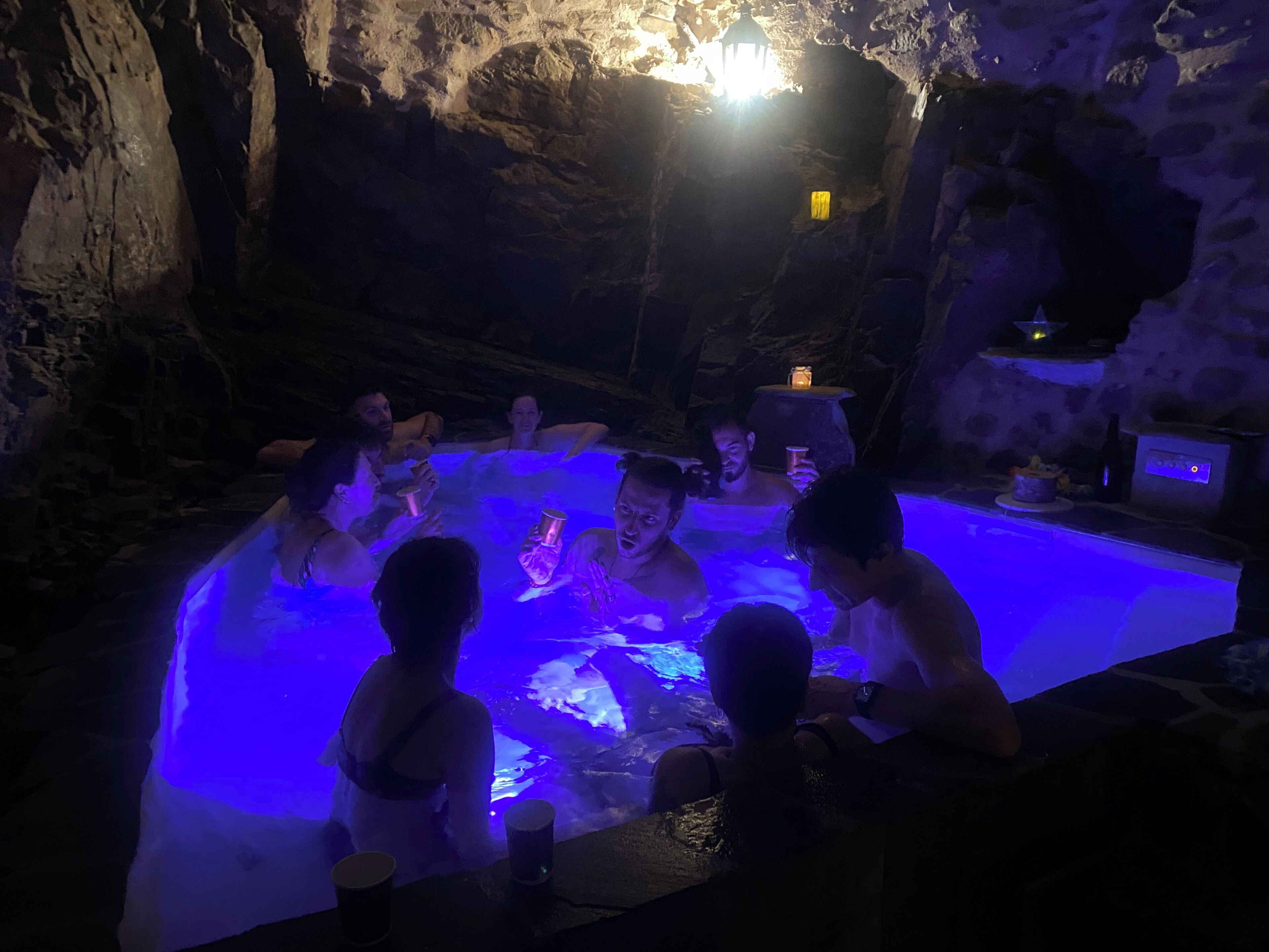 Un grupo de personas en un jacuzzi con iluminación azul, rodeado de paredes rocosas.