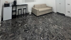 A modern room with a sofa, a TV mounted on the wall, a small kitchenette with a microwave, and a marble floor. - Apartment San Vitaliano-Naples (San Vitaliano)