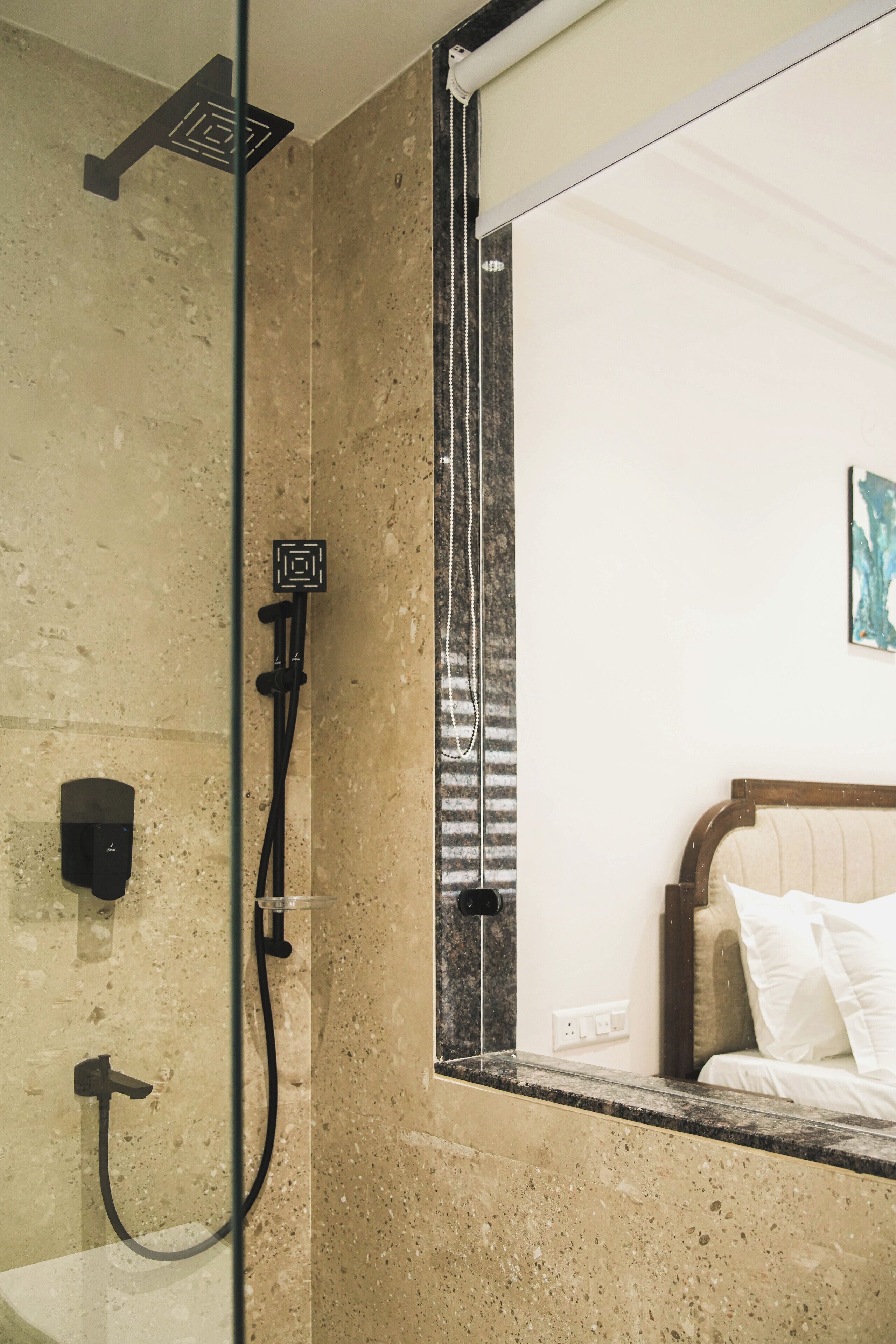 A bathroom with a shower, a mirror, and a bed with white bedding.