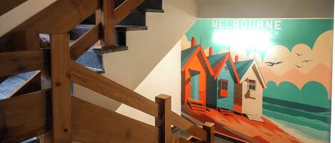 A staircase with wooden railings leading to a room with a mural of houses and a beach scene.