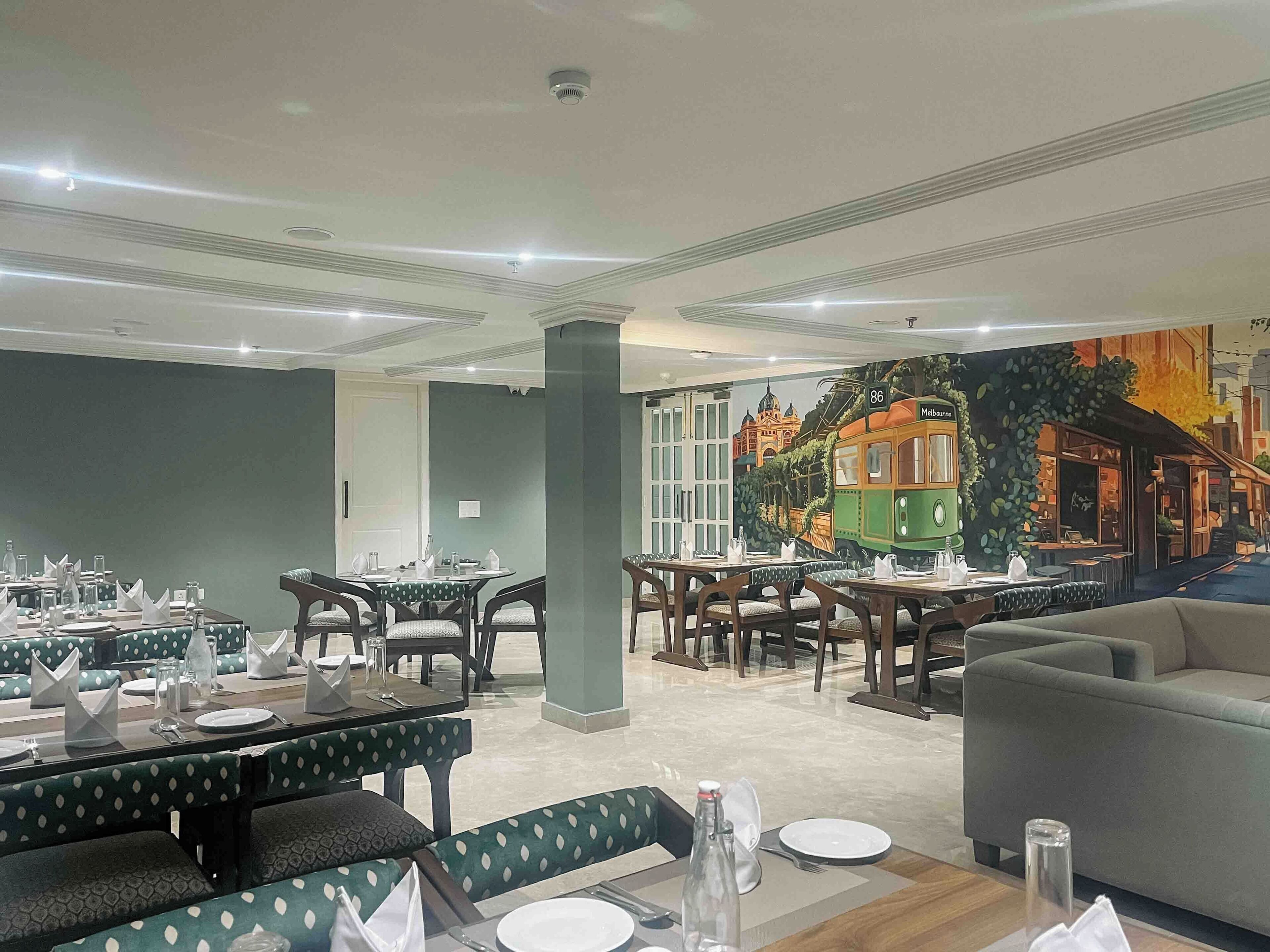 A restaurant with tables set for dining, a mural of a tram, and a green wall.