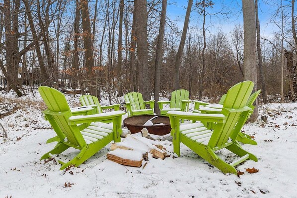 Ein mit Schnee bedeckter Außenbereich mit Sitzgelegenheiten und grünen Adirondack-Stühlen, die um eine Feuerstelle angeordnet sind.