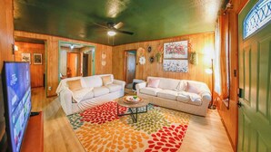 A cozy living room with two white sofas, a colorful rug, and a ceiling fan.