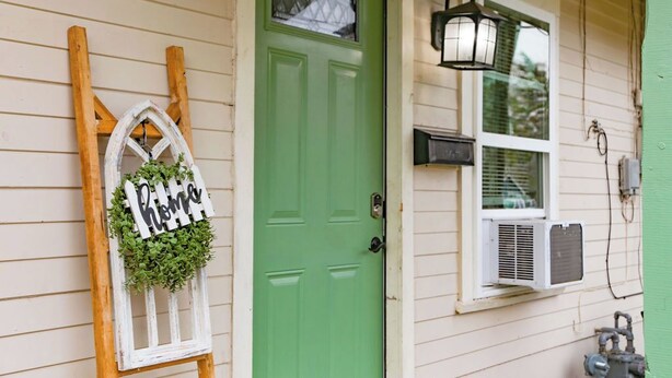 A green door with a white-framed window and a wall-mounted lantern.