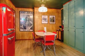 Une cuisine avec un réfrigérateur rouge, une table ronde entourée de chaises rouges et des murs en bois.