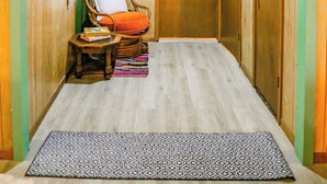 A hallway with wooden walls, a wicker chair, a small table with a book, and a patterned rug.