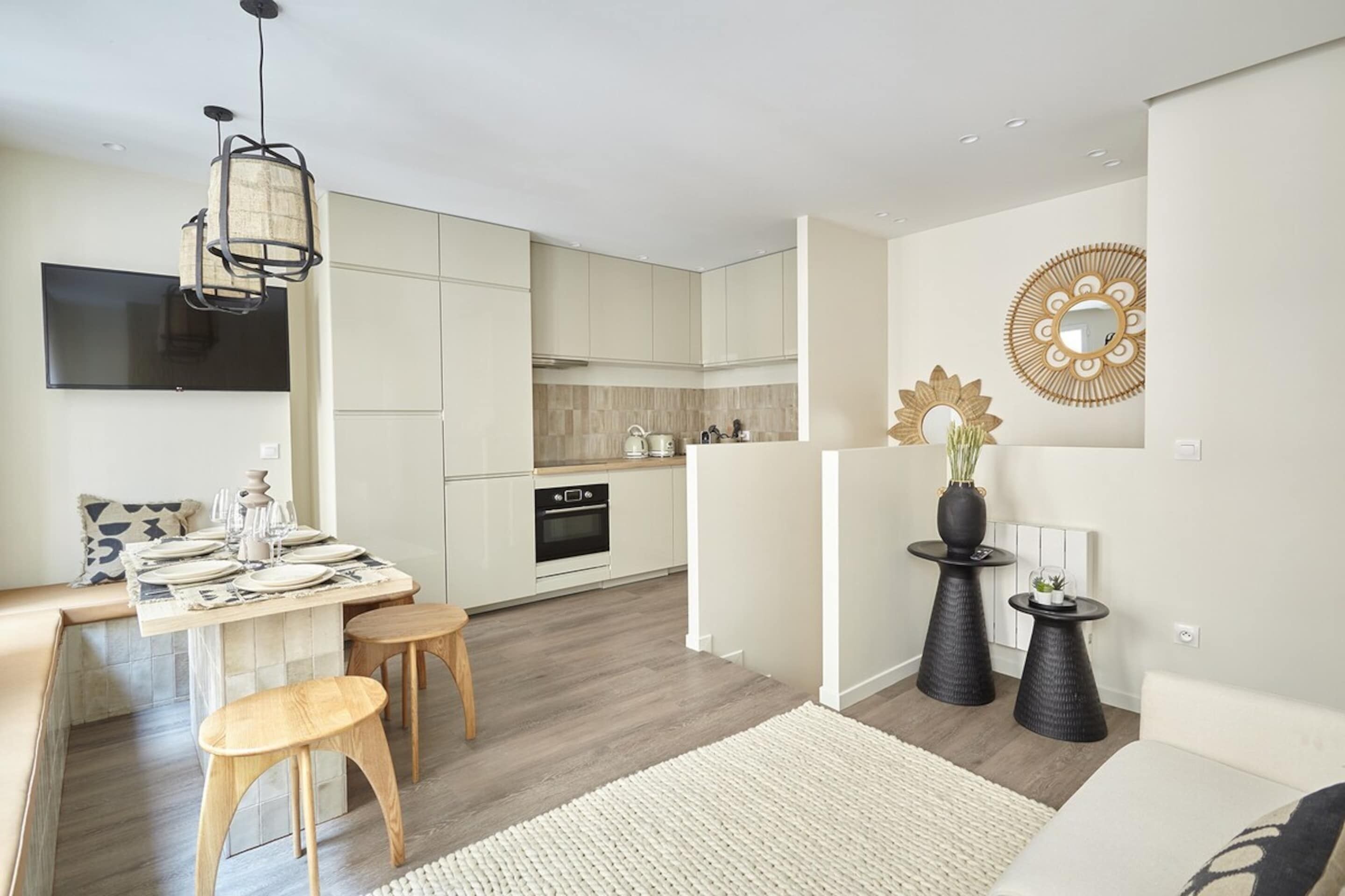 A modern kitchen with white cabinets, a dining area with a table set for four, and a living area with a sofa and decorative vases.