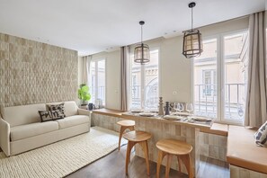 A modern living room with a sofa, a dining area with stools, and a kitchen counter. - Modern 2 Bedrooms Apartment Le Marais/ Beaubourg (Paris)