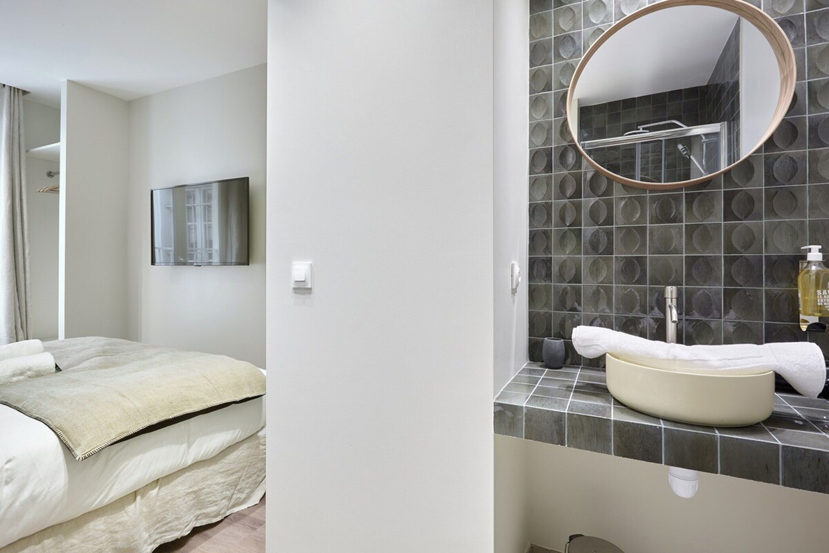 Un baño moderno con un espejo redondo, un lavabo y una ducha.