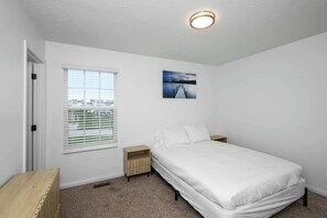 Ein Schlafzimmer mit einem Einzelbett, einem Nachttisch, einem Fenster mit Jalousien und einer Deckenleuchte.