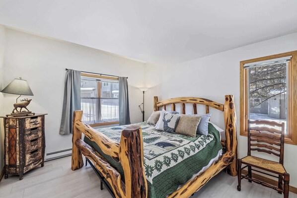 A bedroom with a wooden bed frame, a nightstand, a lamp, and a chair. - Trail Ridge Retreat – Sleeps 8 (Edwards)