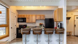A kitchen with wooden cabinets, a black refrigerator, and a microwave. There are three bar stools with metal bases.