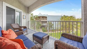 A balcony with wicker furniture, a glass door, and a view of a house and greenery. - Ocean Hibiscus Retreat – For 8 (St. Augustine)