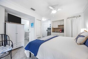 Une chambre comprenant un lit, un bureau, une chaise, une armoire et un coin cuisine.