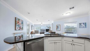 A kitchen with white cabinets, a black countertop, and a dishwasher. There is a window with blinds and a ceiling fan. - Ocean Hibiscus Retreat – For 8 (St. Augustine)