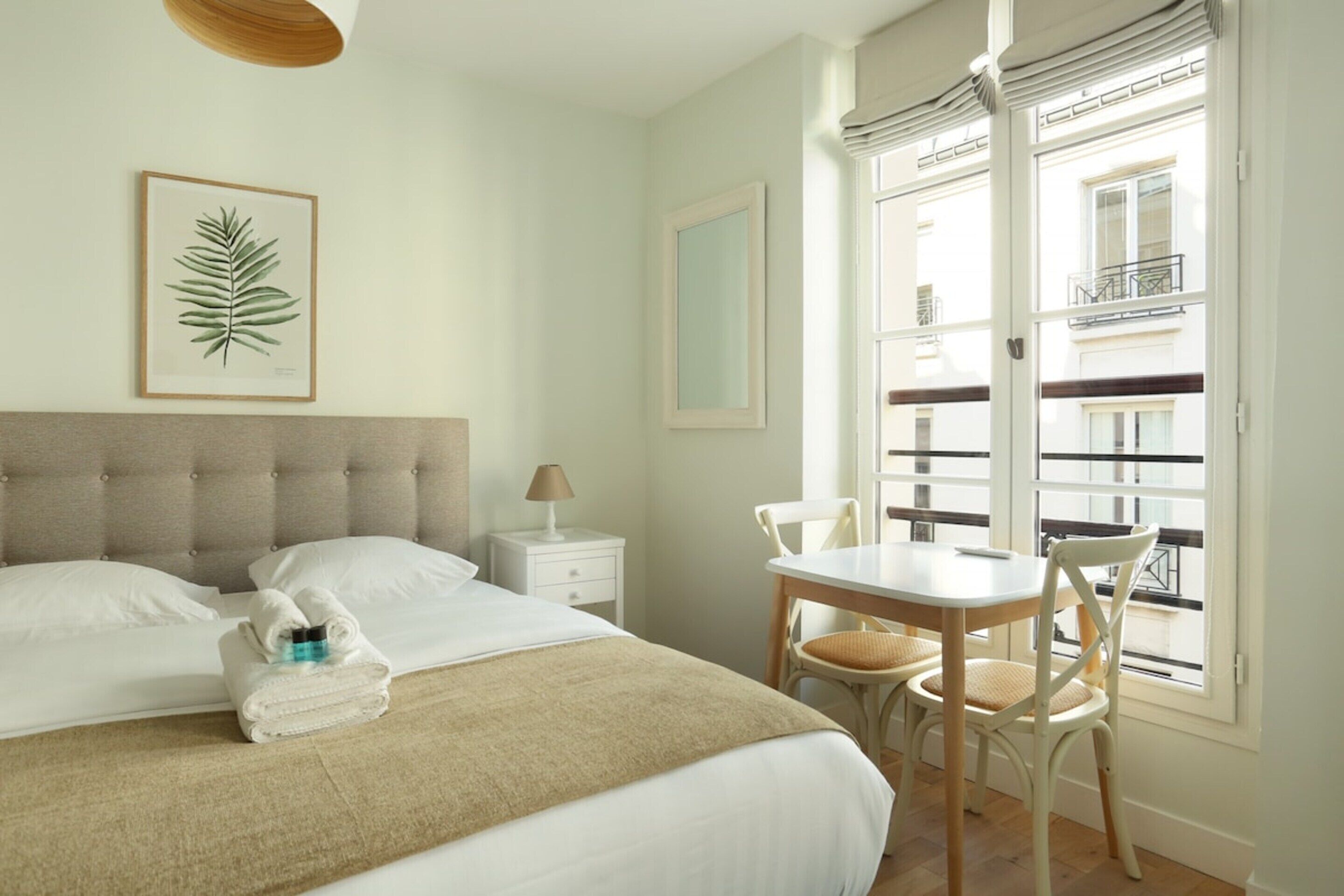 A bedroom with a bed, bedside table, lamp, and a view of the outside balcony.