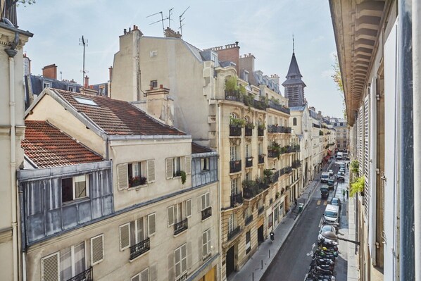 A narrow street lined with multi-story buildings, some with balconies and a church spire in the distance.