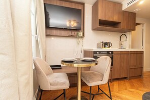 Une cuisine moderne avec des meubles en bois, un téléviseur à écran plat et une table ronde accompagnée de deux chaises.