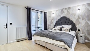 Un dormitorio moderno con una cama grande, un radiador, una ventana con cortinas y una pared con un diseño geométrico.