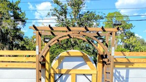 A wooden gate with a white door, flanked by two planters with plants labeled "Meet Petit!" - Great place to meet up (Gainesville)