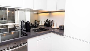 A modern kitchen with white cabinets, a black countertop, and stainless steel appliances including a coffee maker, toaster, and kettle. - Charming Studio Paris / Le Marais (Paris)