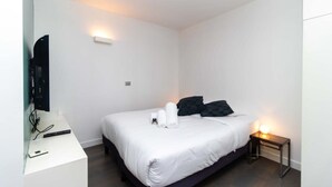 A modern hotel room with a neatly made bed, a bedside table with a lamp, and a flat-screen TV mounted on the wall. - Charming Studio Paris / Le Marais (Paris)